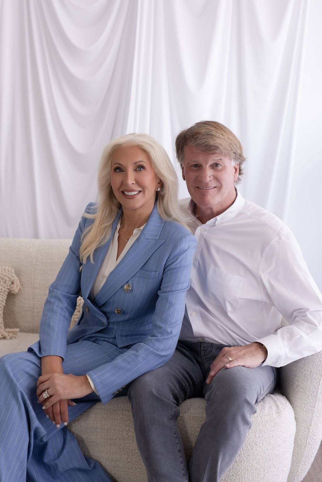 Dr. Tracey Skale and Dr. Paul Keck seated together on a cream sofa in front of a white drape